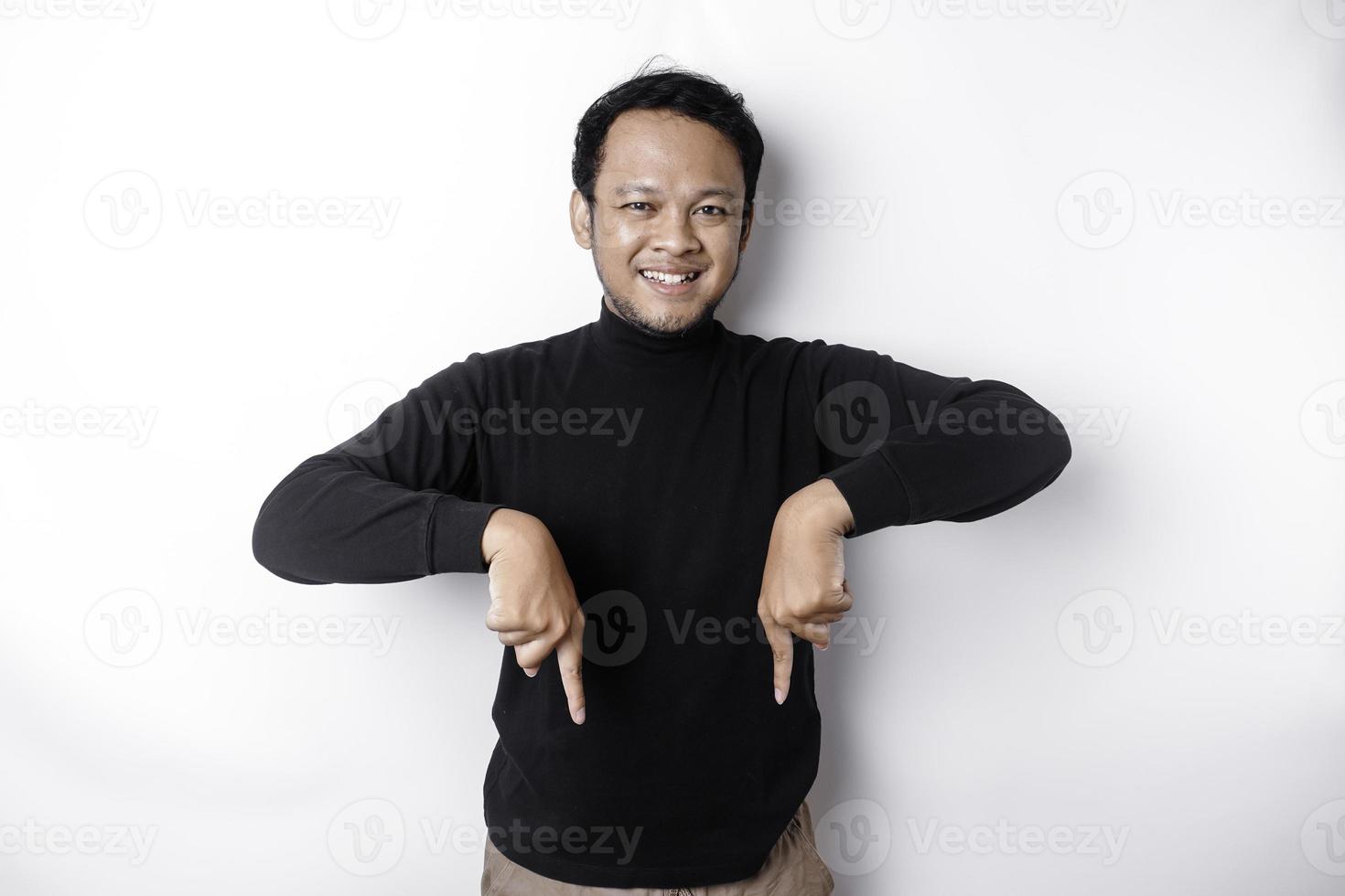 aufgeregt asiatisch Mann tragen schwarz Hemd zeigen beim das Kopieren Raum unten ihn, isoliert durch Weiß Hintergrund foto