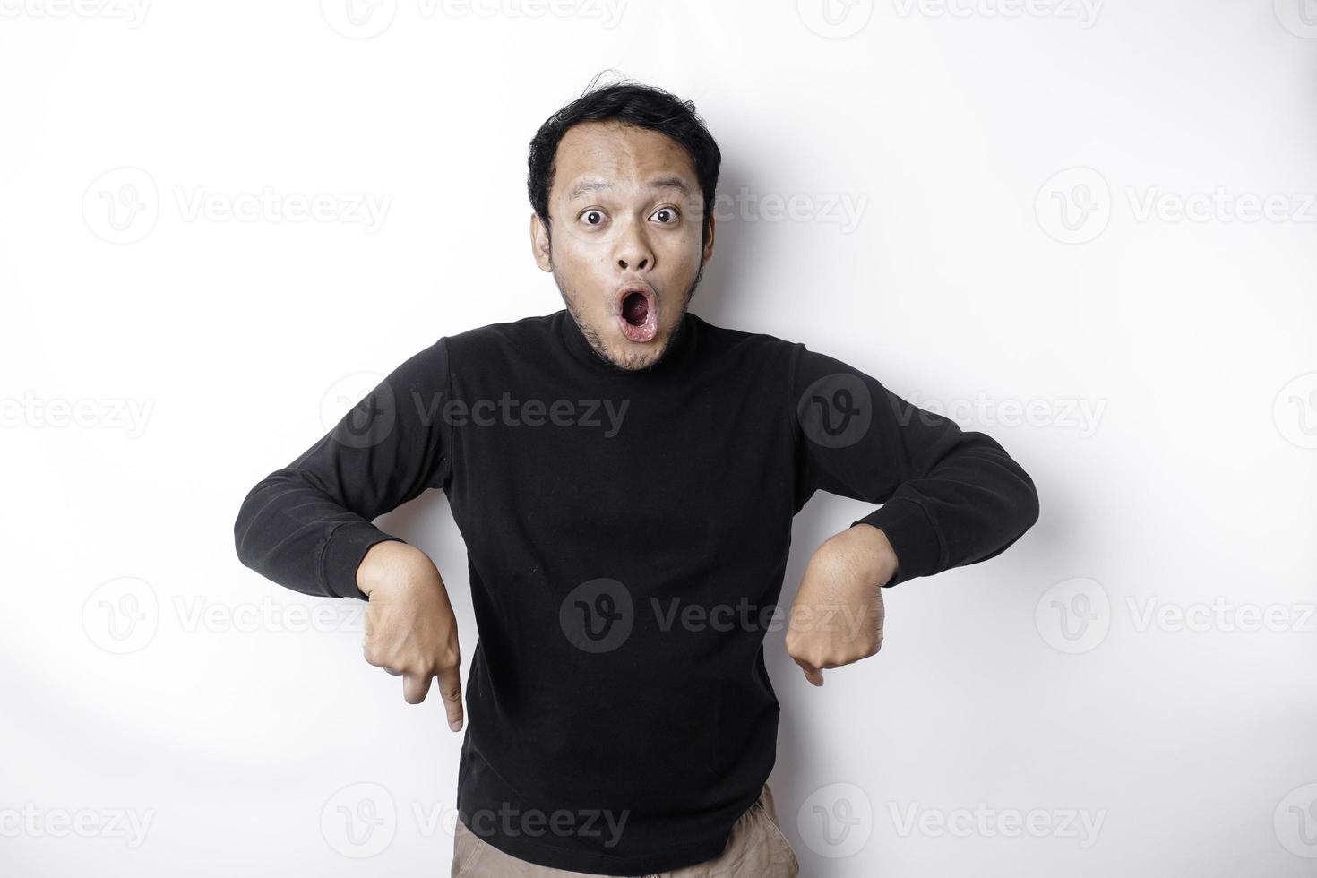 schockiert asiatisch Mann tragen schwarz Shirt, zeigen beim das Kopieren Raum unten ihn, isoliert durch Weiß Hintergrund foto