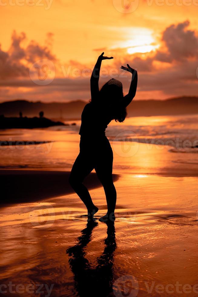 ein asiatisch Frau im Silhouette ist tun Gymnastik- Bewegungen sehr agil auf das Strand Sand foto