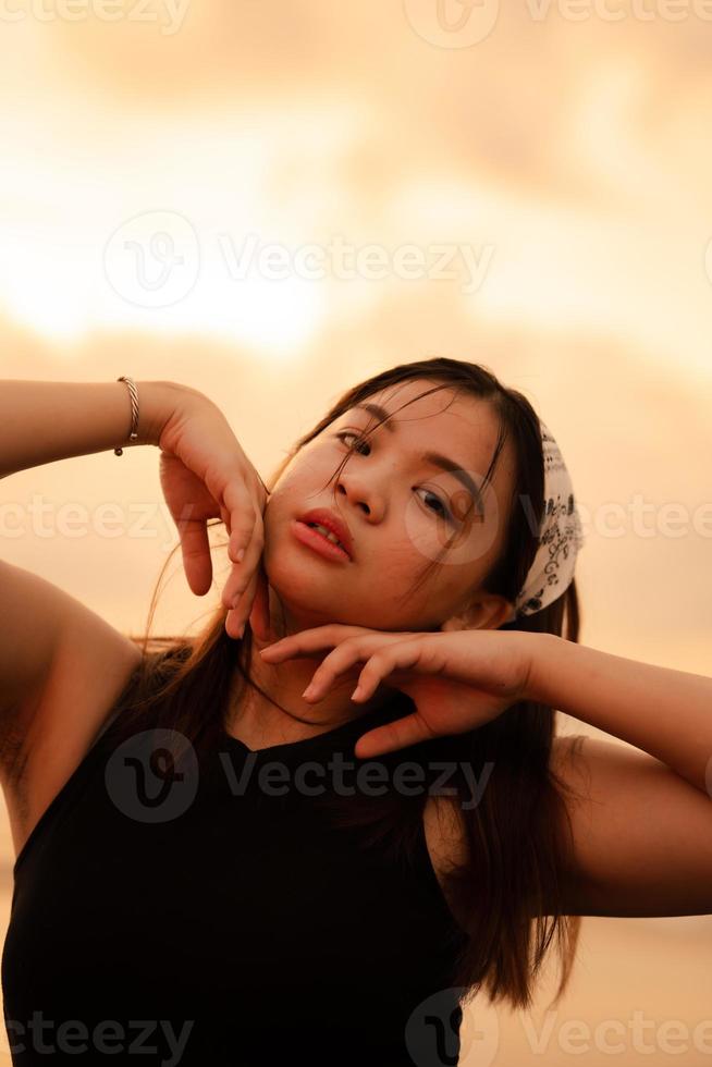 ein asiatisch Teenager tragen ein Weiß Bandana und schwarz Hemd mit ein sexy Ausdruck auf das Strand Sand foto