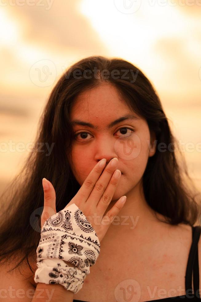 ein asiatisch Frau mit lange schwarz Haar posiert mit ihr Hände während genießen das Aussicht von das Strand foto
