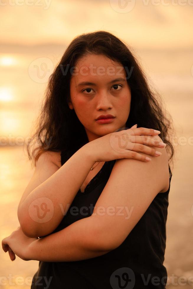 ein asiatisch Frau im ein schwarz Kleid und rundlich Körper Streiks ein sehr kokett Pose während genießen das Strand foto