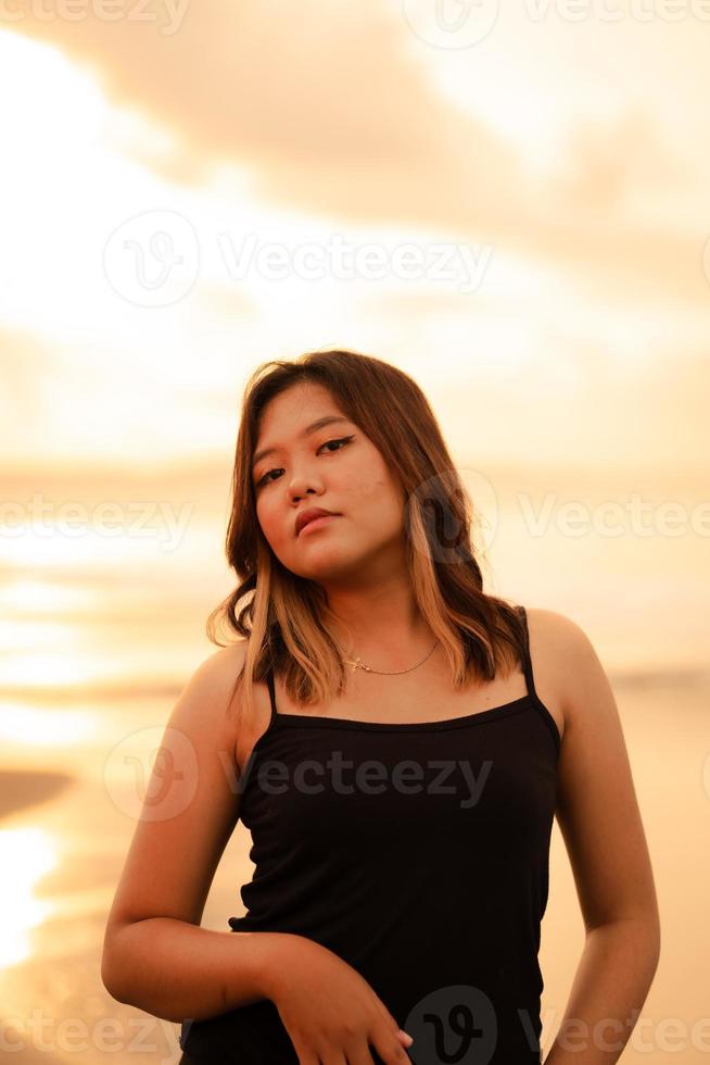 ein blond asiatisch Frau mit ein schön Gesicht und schwarz Kleider genießen das Schönheit von das Strand und das Wellen im das Morgen foto