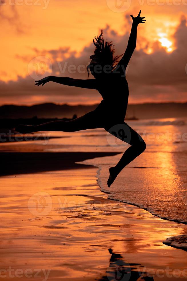 ein balinesisch Frau im das bilden von ein Silhouette führt aus Ballett Bewegungen sehr geschickt und flexibel auf das Strand mit das Wellen abstürzen foto