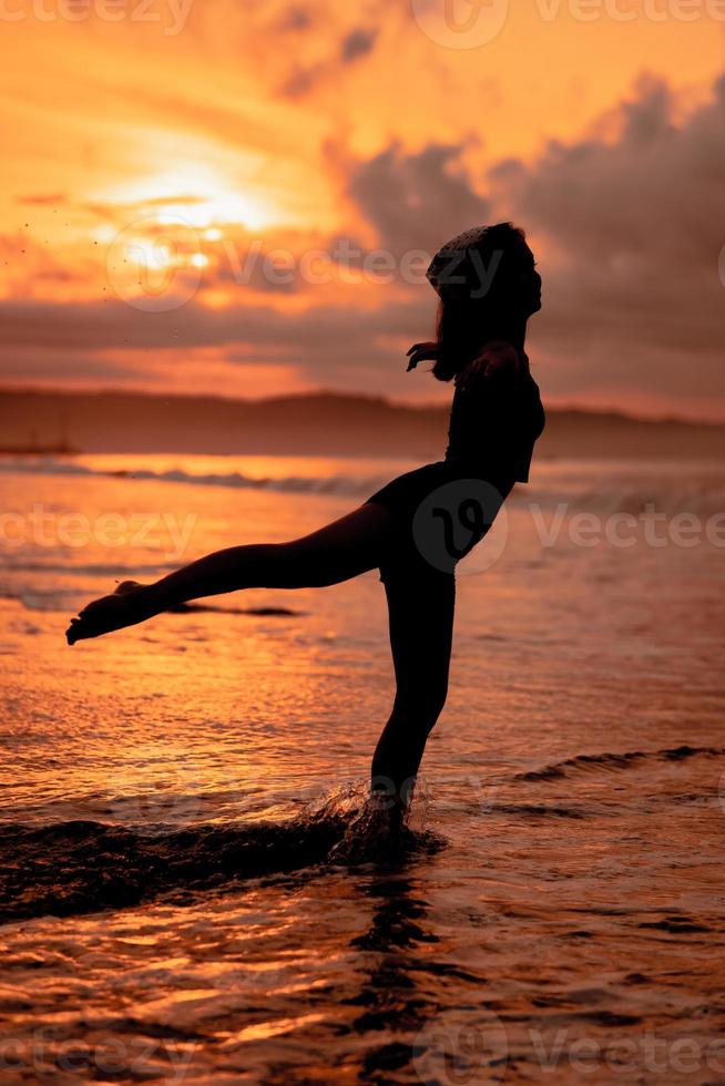 Silhouette von ein asiatisch Frau üben ihr Ballett bewegt sich auf das Strand mit das Wellen abstürzen Vor das Festival beginnt foto