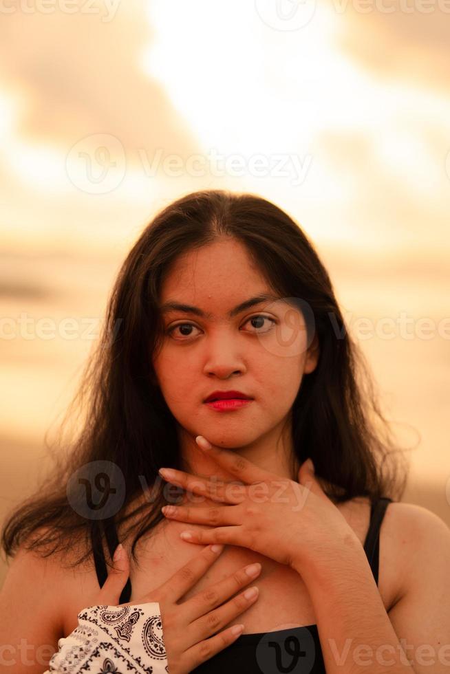 ein asiatisch Frau mit schwarz Haar und ein schön Gesicht posieren im Vorderseite von das Strand mit warm foto