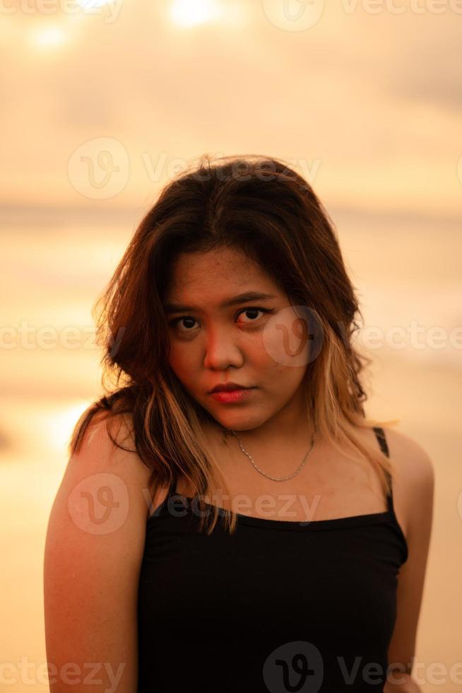 ein Porträt von ein asiatisch Frau im ein schwarz Kleid tun ein sexy Pose während genießen das Aussicht in der Nähe von das Strand foto