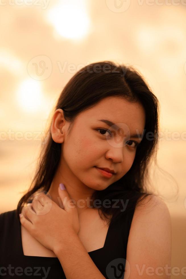 schön asiatisch Frau mit ein schwarz Hemd und schwarz Haar lächelnd mit glatt Haut in der Nähe von das Strand foto