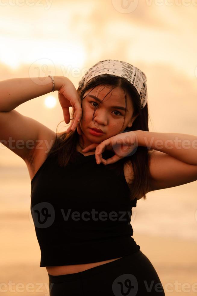 ein asiatisch Teenager tragen ein Weiß Bandana und schwarz Hemd mit ein sexy Ausdruck auf das Strand Sand foto