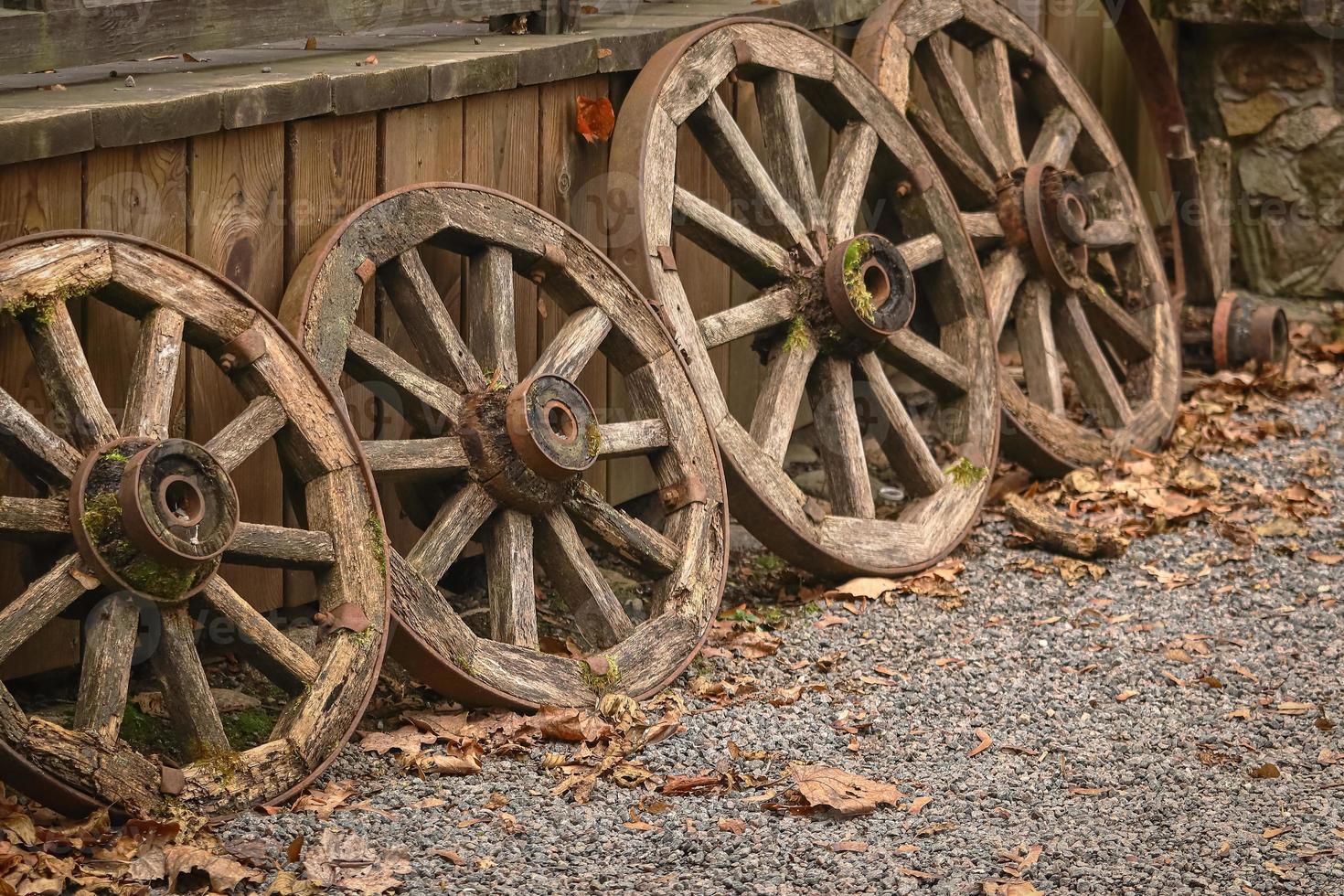 alt hölzern Räder vereinbart worden im ein Reihe in der Nähe von hölzern Planke Elevation auf Kieselstein Straße mit Herbst Blätter foto