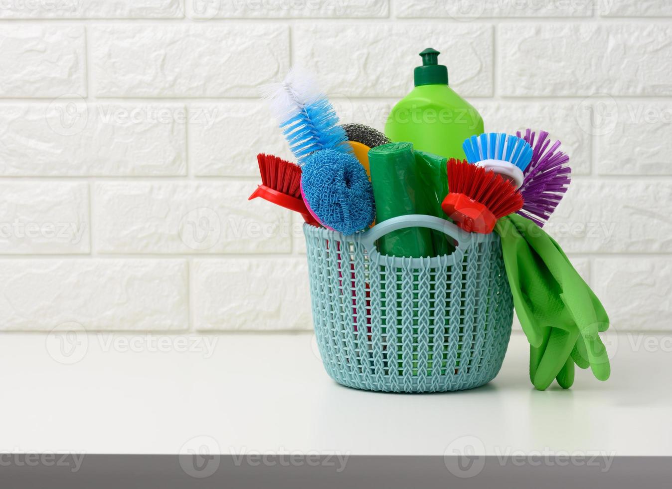 Plastik Korb mit Bürsten, Desinfektionsmittel im ein Flasche, Gummi Handschuhe auf das Hintergrund von ein Weiß Backstein Mauer. Haus Reinigung Artikel einstellen foto