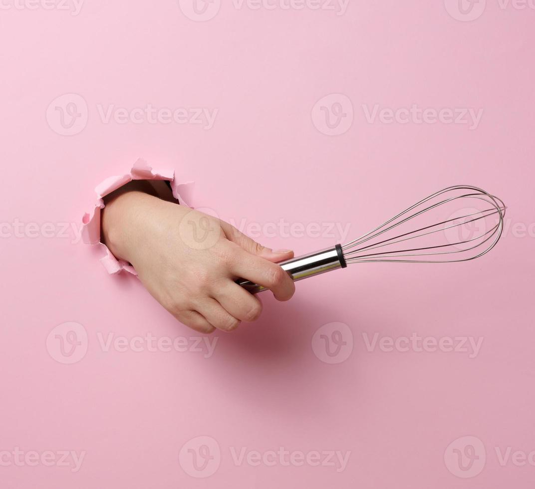 weiblich Hand hält ein Metall Schneebesen zum Prügel Produkte auf ein Rosa Hintergrund foto