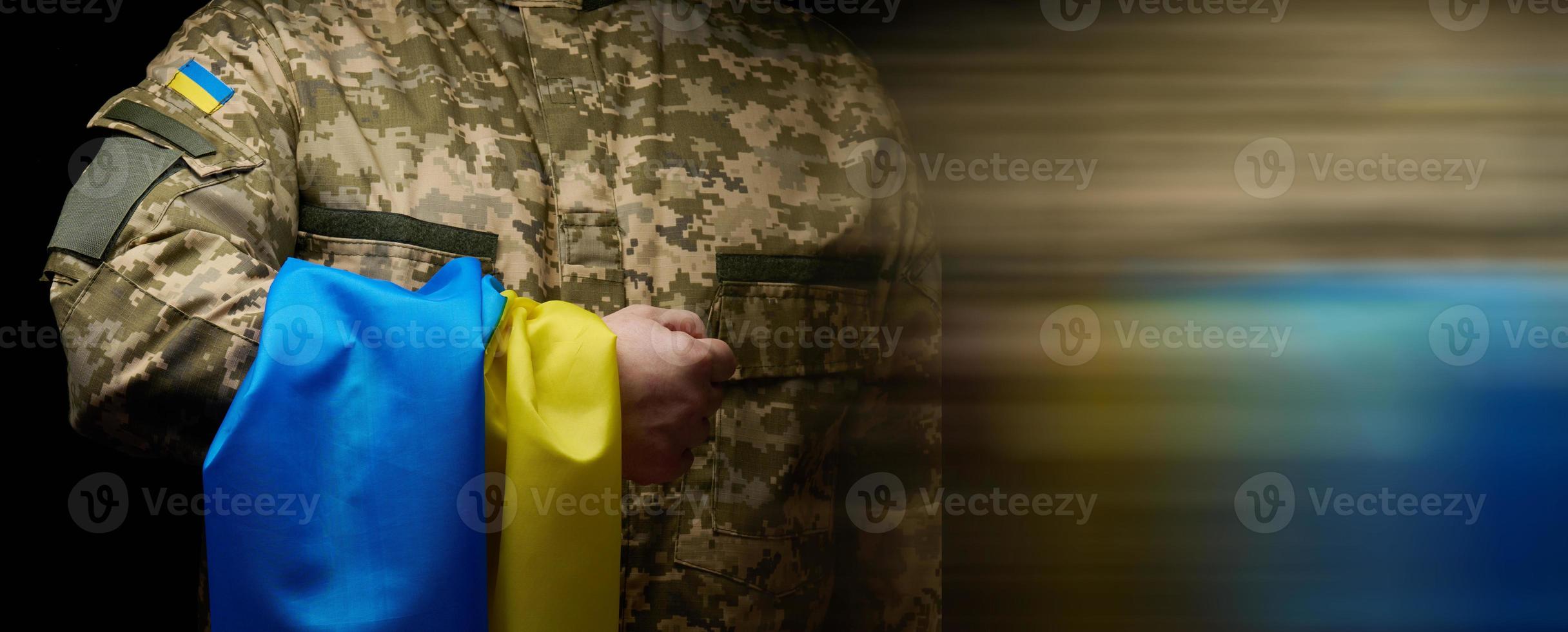 ein Soldat von das ukrainisch bewaffnet Kräfte steht mit ein Blau Gelb Flagge von Ukraine auf ein schwarz Hintergrund. Auszeichnung Veteranen und Gedenken jene getötet im das Krieg foto