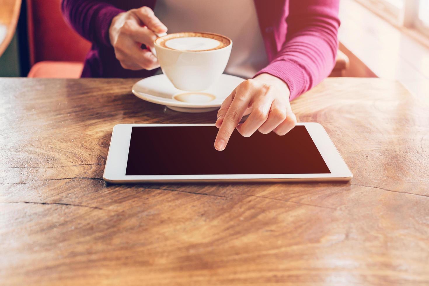 Hand Frau Berührungssensitiver Bildschirm Tablette Computer und Tasse im Kaffee Geschäft mit Jahrgang Ton. foto