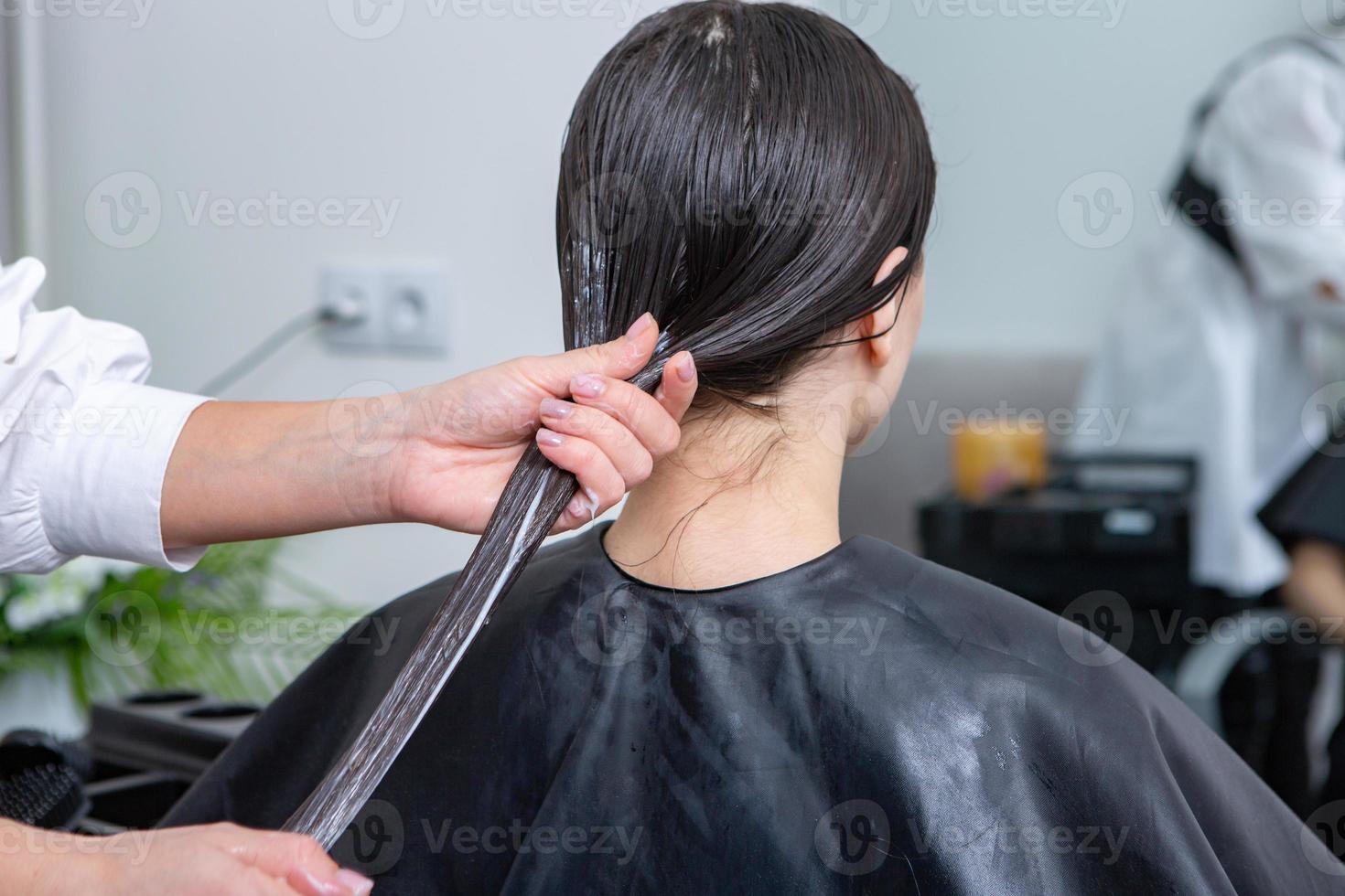 Friseur wendet eine Haarmaske auf glattes schwarzes Haar an. Haarpflege im Schönheitssalon. foto