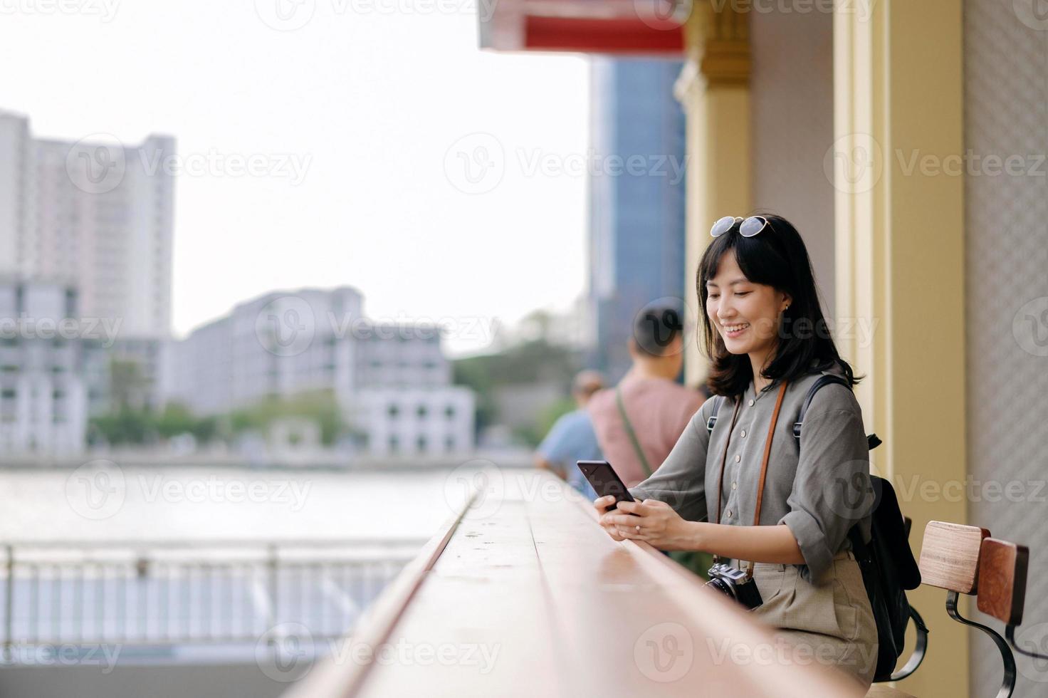 jung asiatisch Frau Rucksack Reisender mit Handy, Mobiltelefon Telefon im ausdrücken Boot Seebrücke auf Chao Phraya Fluss im Bangkok. foto