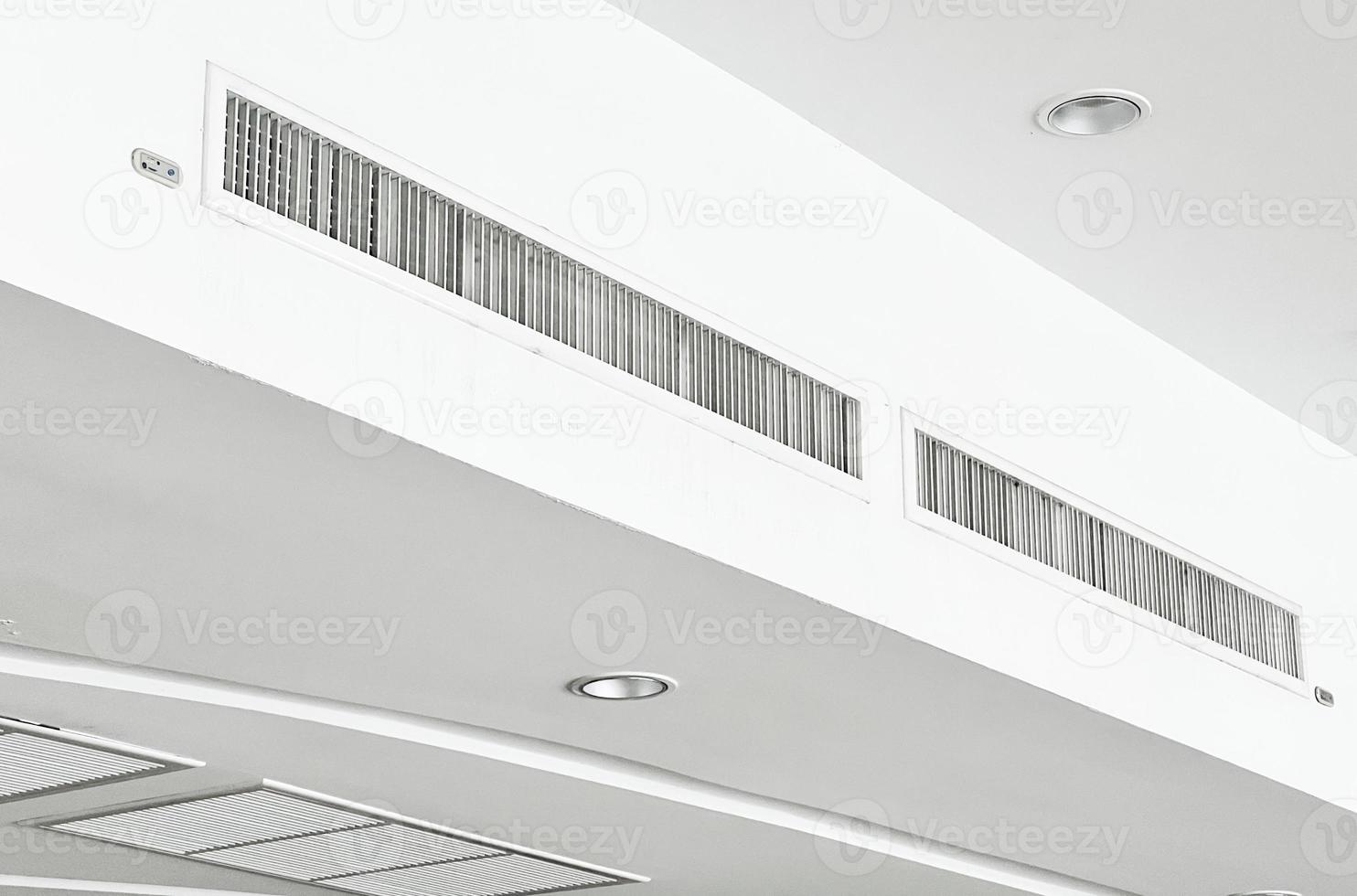 Deckenmontierte Kassettenklimaanlage und modernes Lampenlicht an weißer Decke. Kanalklimaanlage für Zuhause oder Büro foto