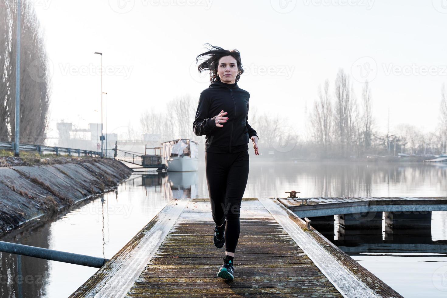 jung Erwachsene Frau ist Laufen auf ein Hafen Kai im das Morgen foto
