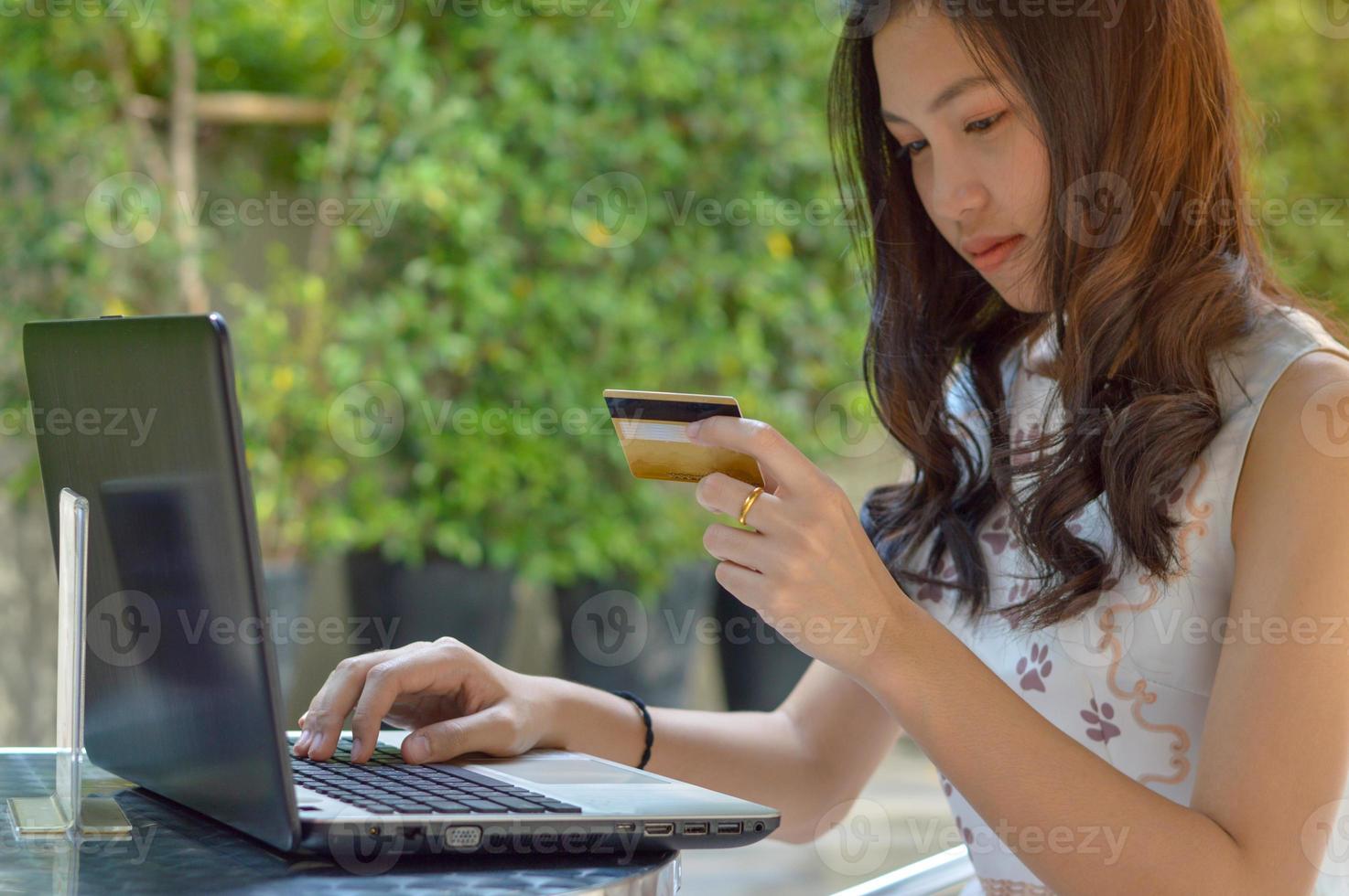 asiatisches Mädchen, das Kreditkarte hält und Laptop verwendet foto