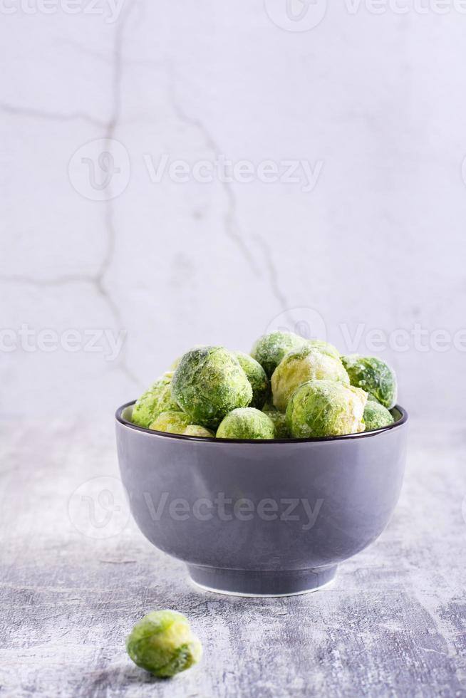 gefroren Brüssel Sprossen im ein Schüssel auf ein grau Hintergrund. Vegetarier Lebensmittel. Vertikale Aussicht foto