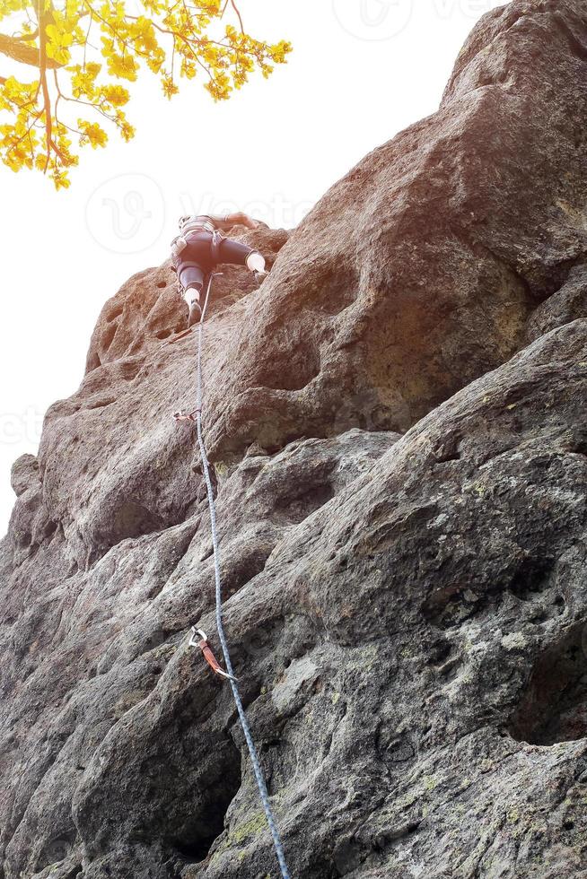 männlich Bergsteiger, jung Männer-Kletterer Klettern ein schwierig Route auf ein Cliff. Bergsteiger klettert ein felsig Mauer. mit Sicherheit Seil auf das Felsen foto