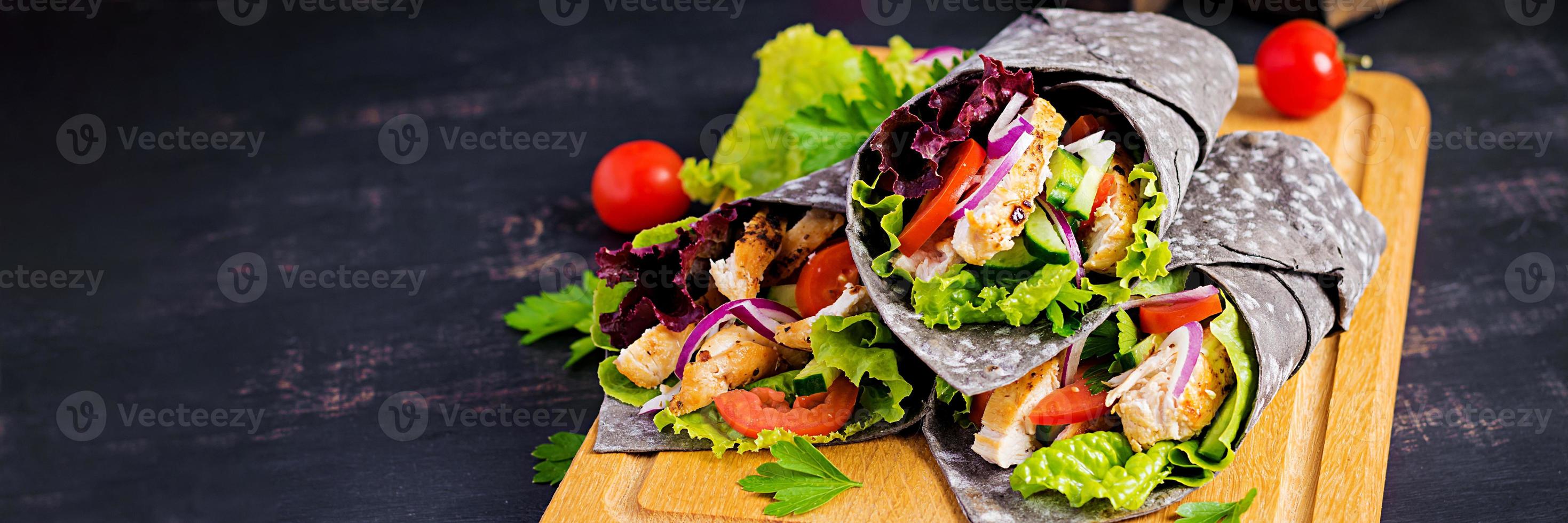 Tortilla mit hinzugefügt Tinte Tintenfisch Wraps mit Hähnchen und Gemüse auf schwarz Hintergrund. Hähnchen Burritos, Mexikaner Lebensmittel. Banner foto