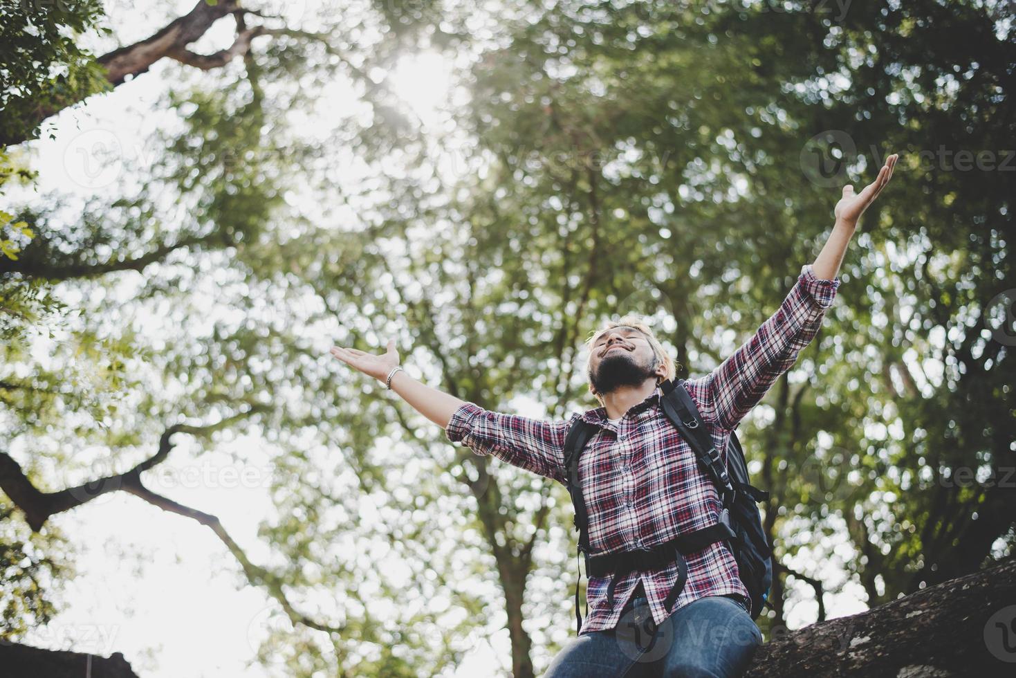 junger Wanderer-Hipster-Mann, der auf einem Ast mit ausgestreckten Armen sitzt foto