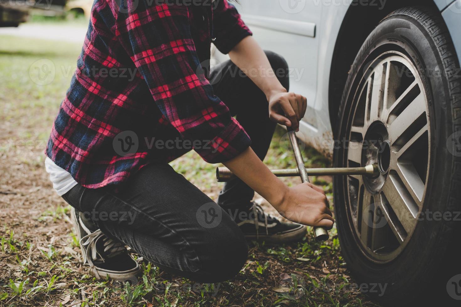 junge Hipster-Frau, die einen platten Reifen auf ihrem Auto auscheckt foto