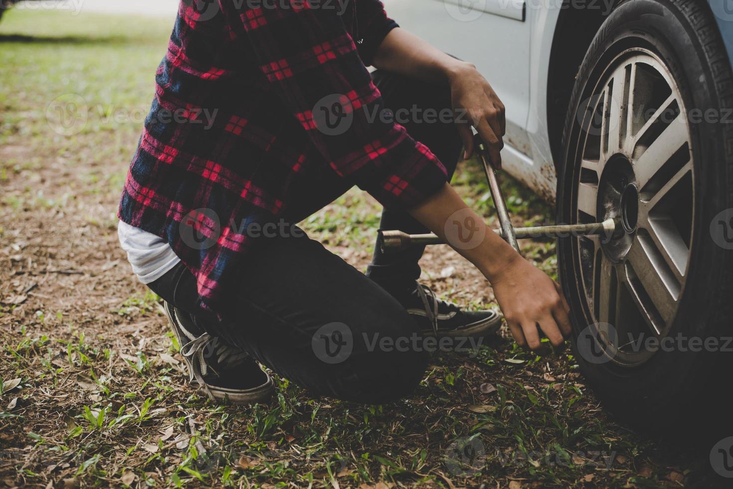 junge Hipster-Frau, die einen platten Reifen auf ihrem Auto auscheckt foto