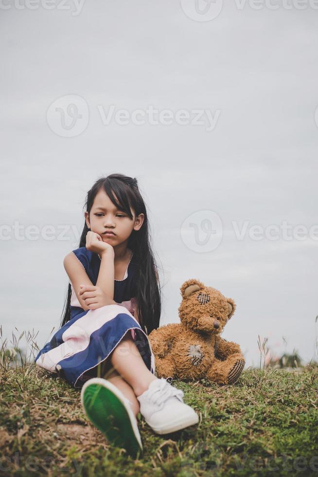 süßes asiatisches Mädchen mit Teddybär, der in einem Feld sitzt foto