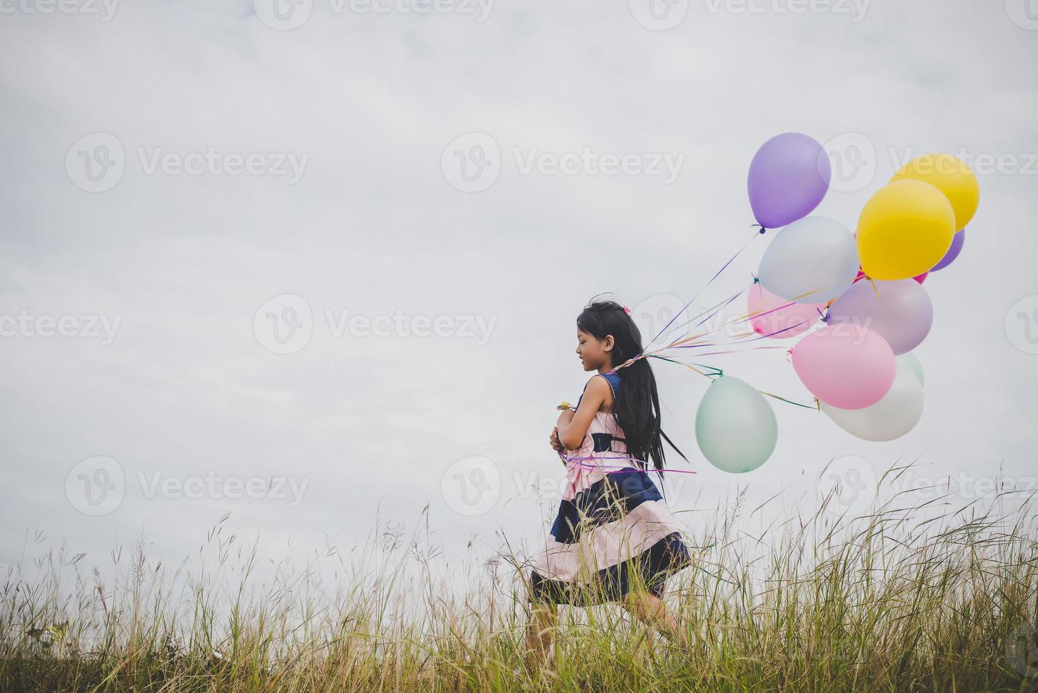 kleines Mädchen, das mit Luftballons auf Wiesenfeld spielt foto