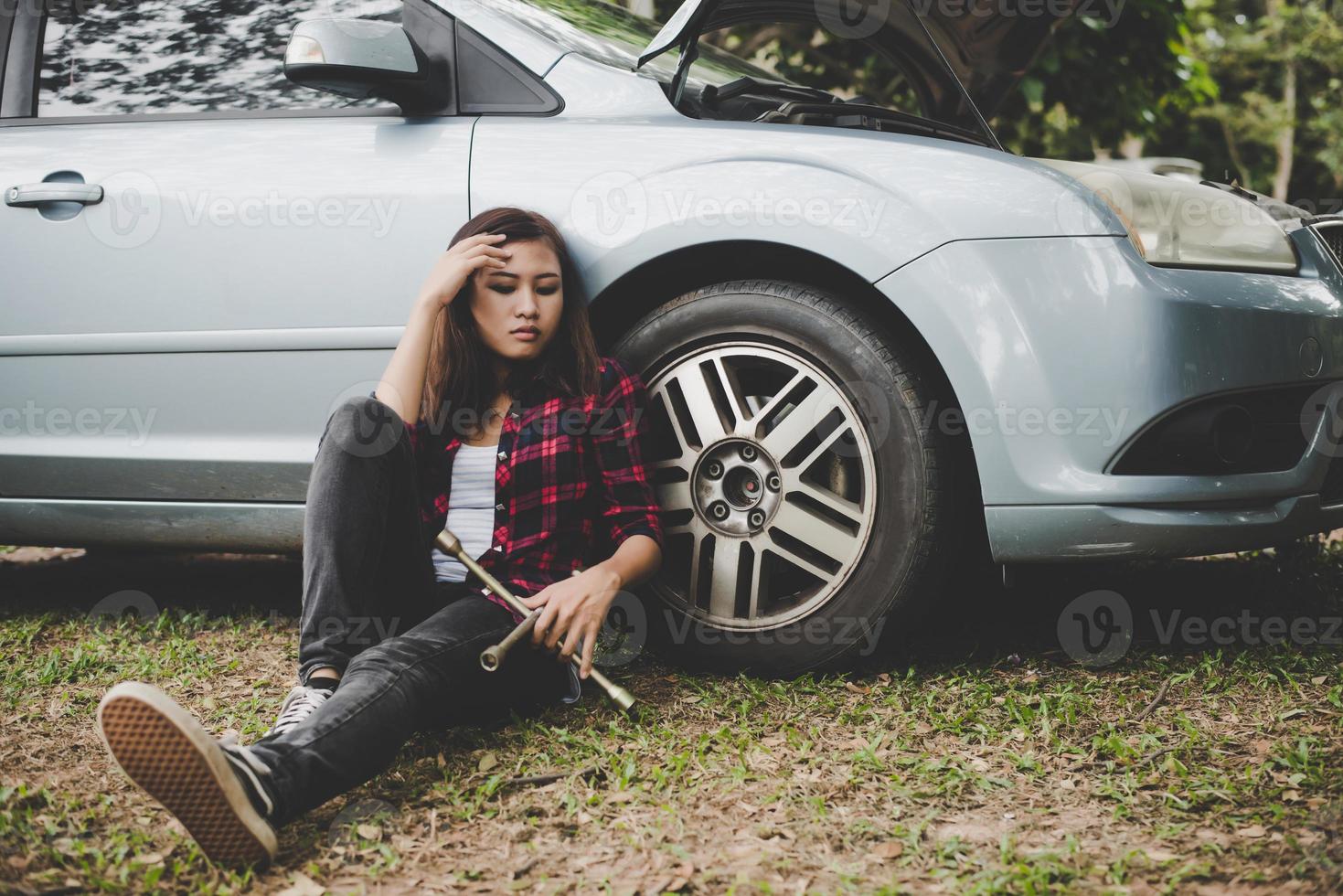 junge Hipsterfrau mit einem platten Reifen auf ihrem Auto foto