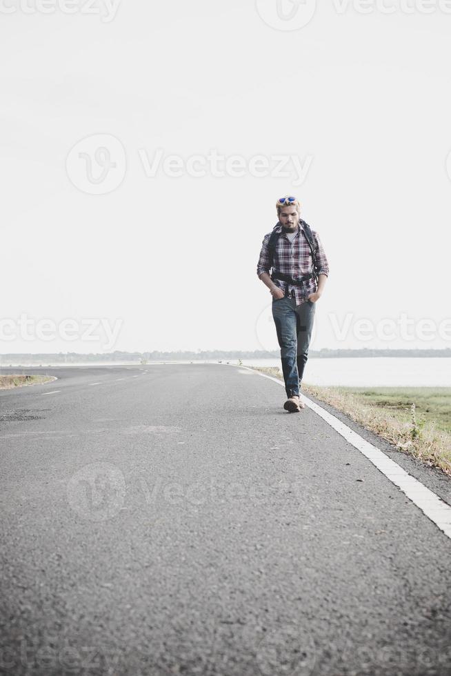 junger Touristenmann, der auf einer Landstraße geht foto