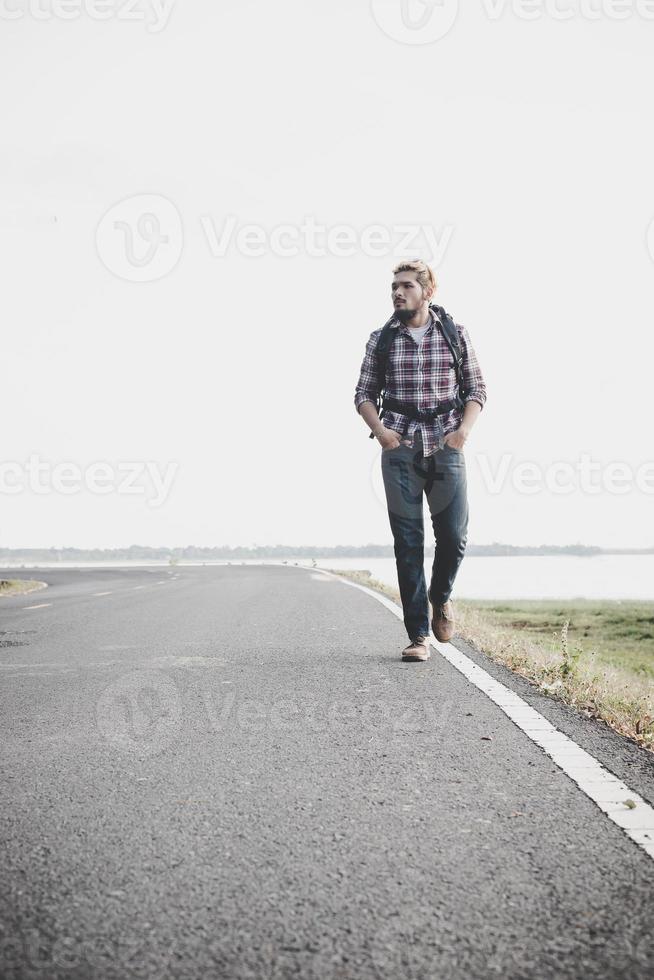 junger Touristenmann, der auf einer Landstraße geht. foto