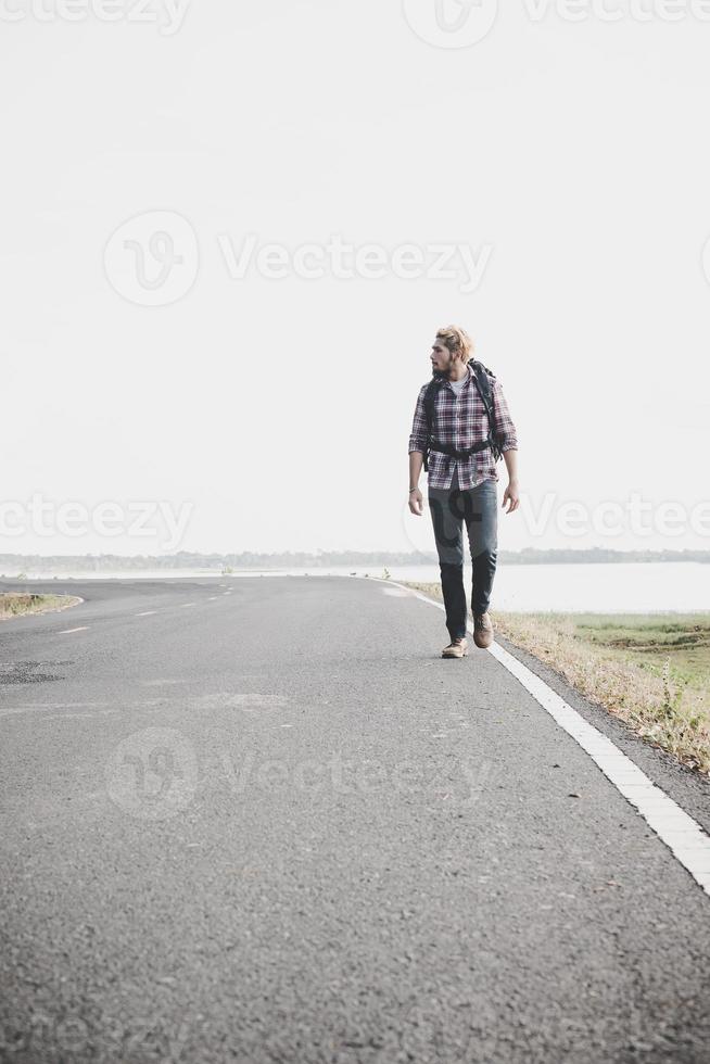 junger Touristenmann, der auf einer Landstraße geht foto