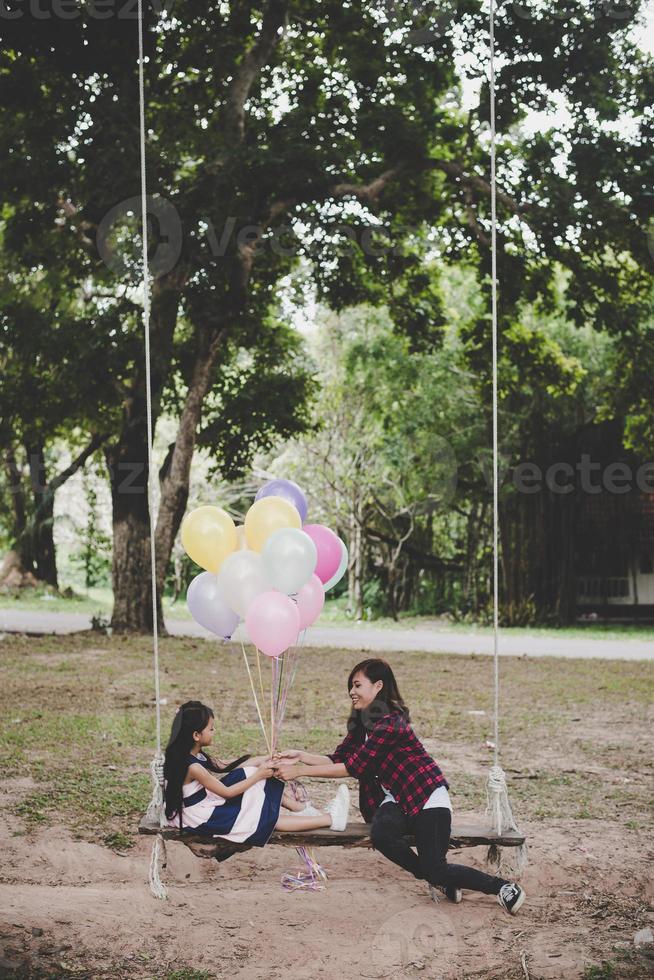 Mutter mit Tochter sitzt auf Schaukel mit bunten Luftballons foto