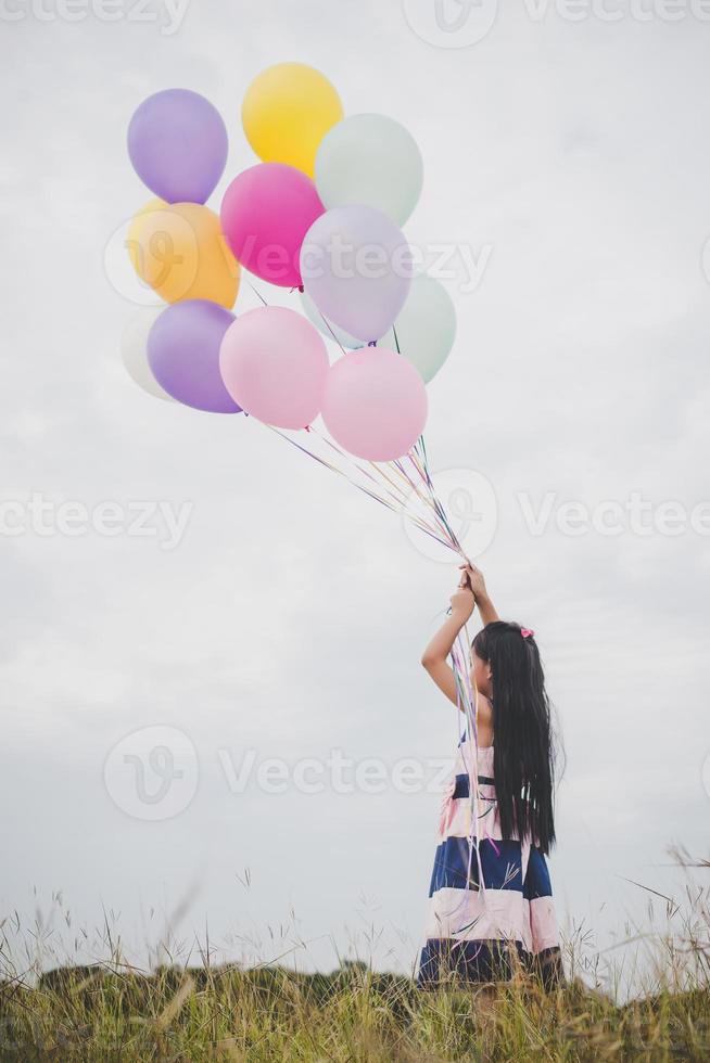 kleines Mädchen, das mit Luftballons auf Wiesenfeld spielt foto