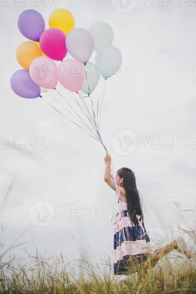 kleines Mädchen, das mit Luftballons auf Wiesenfeld spielt foto