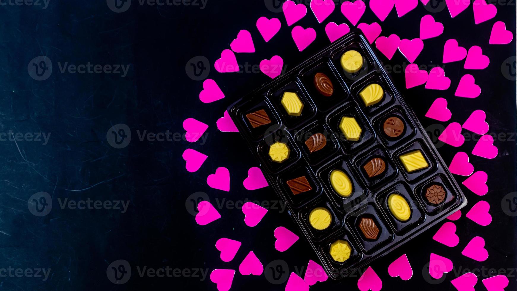 köstliche Schokolade, umgeben von rosa Herzen auf schwarzem Hintergrund foto