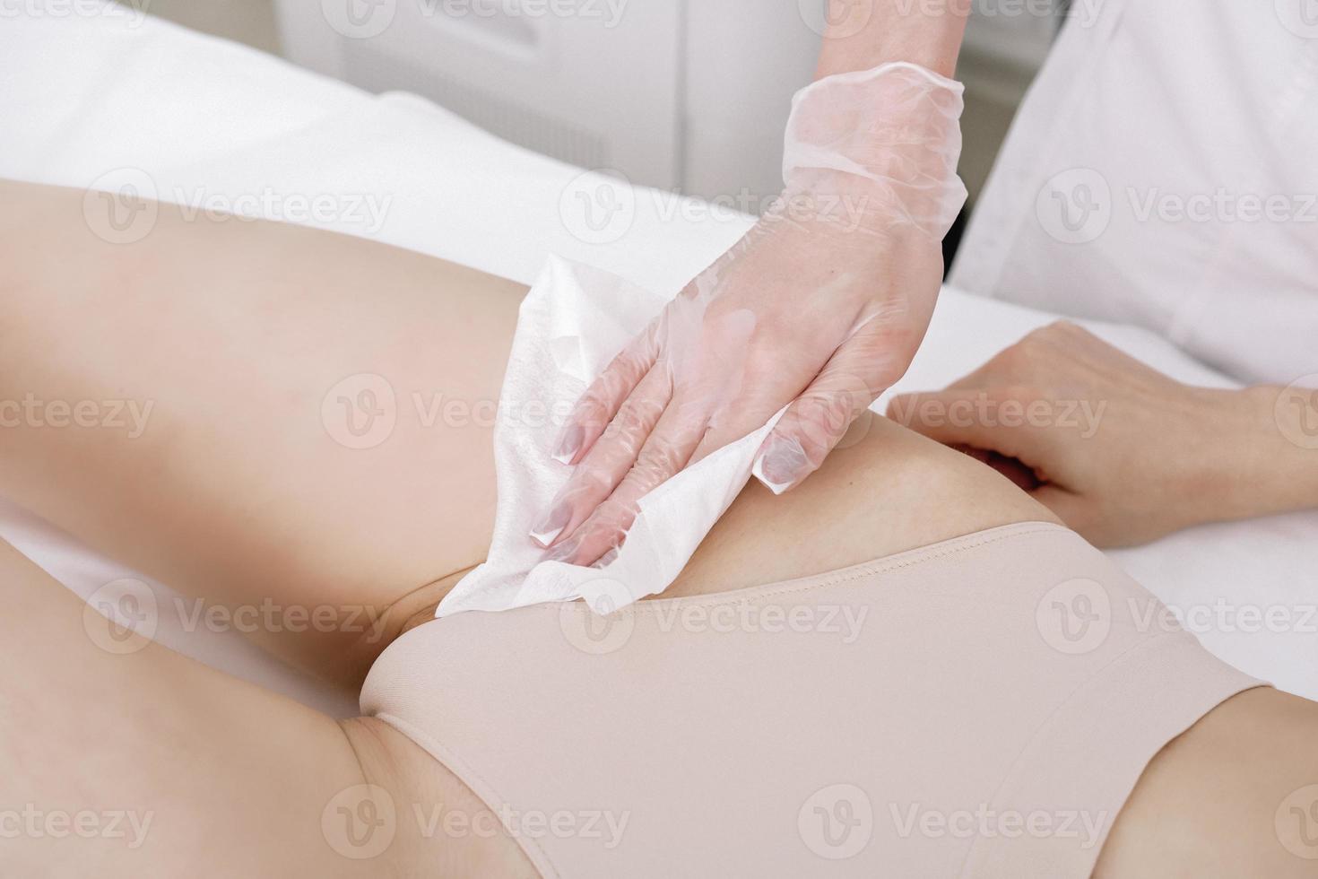 Kosmetikerin tragen medizinisch Handschuhe entfernt Agent Gel von das Kunden Bikini Bereich. schließen hoch. Haar Entfernung im ein Fachmann Schönheit Salon foto