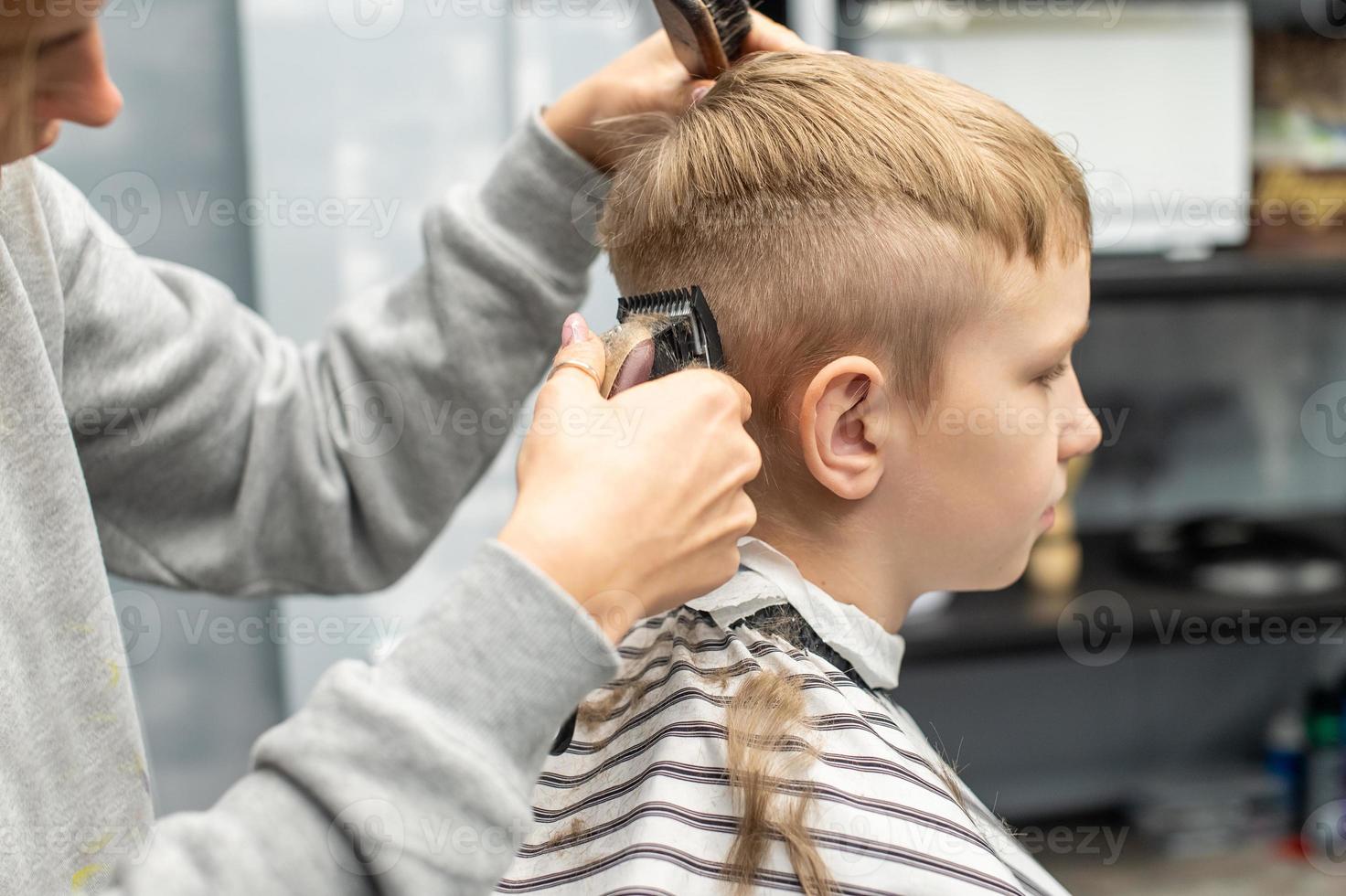 ein Junge ist Sitzung im ein Barbier Geschäft, Schneiden seine Haar mit ein Clipper foto