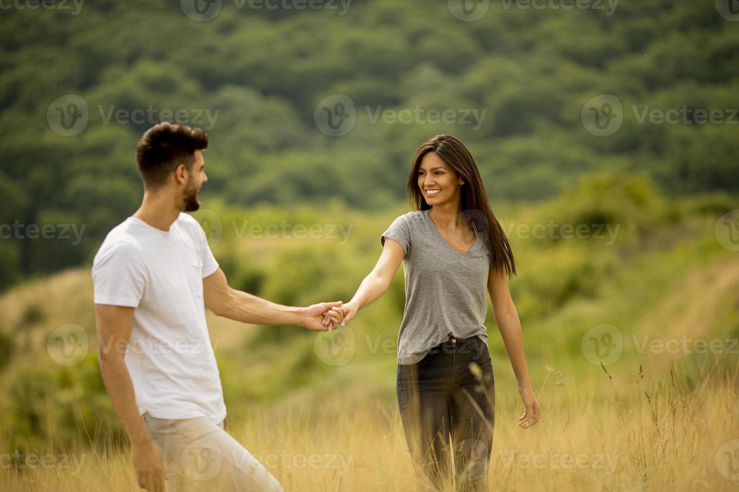 glückliches junges Paar in der Liebe, die durch Grasfläche geht foto
