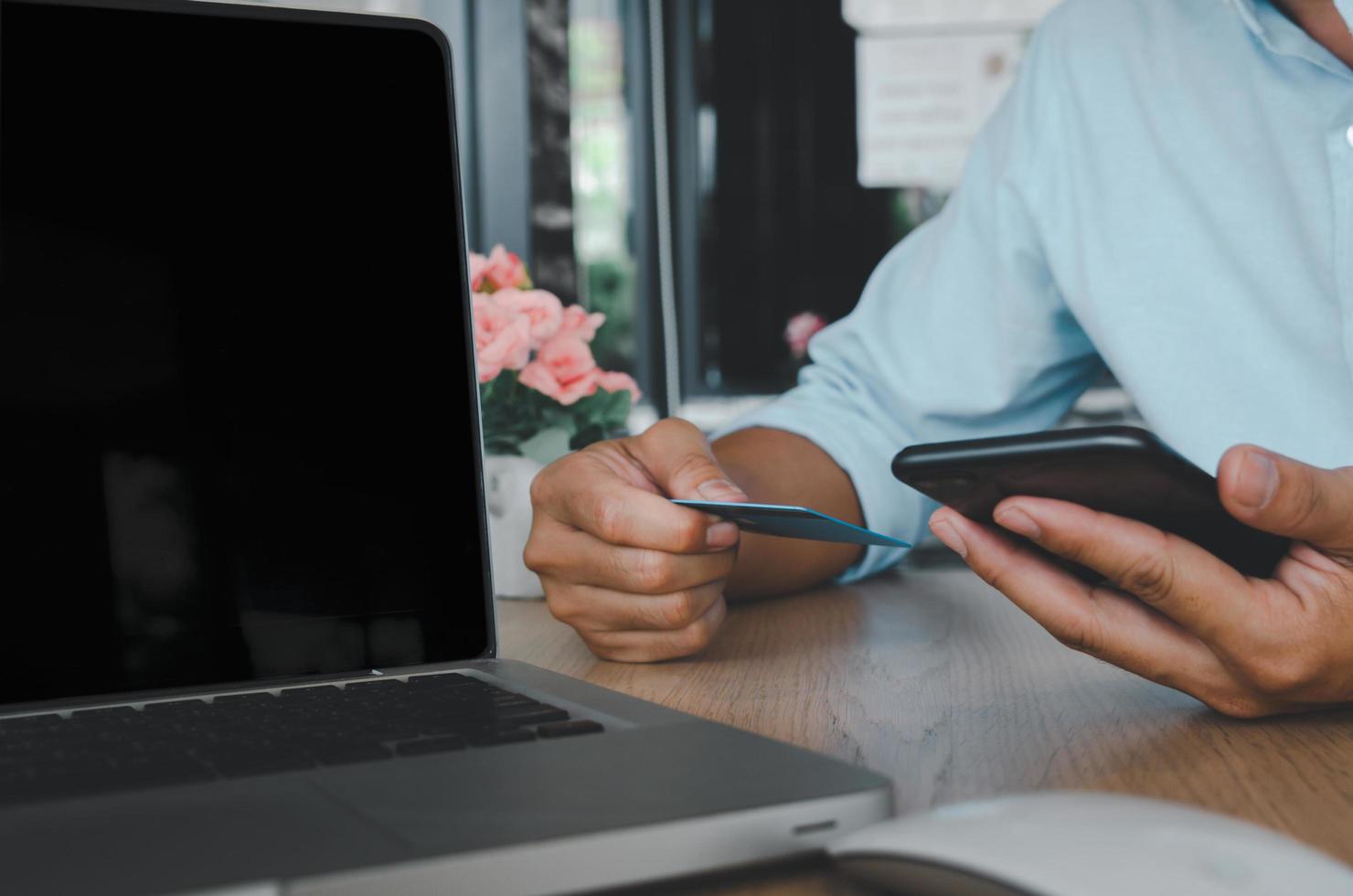 Geschäftsmann, der ein mobiles Smartphone und eine Kreditkarte mit einem Computer-Laptop auf dem Tisch verwendet foto