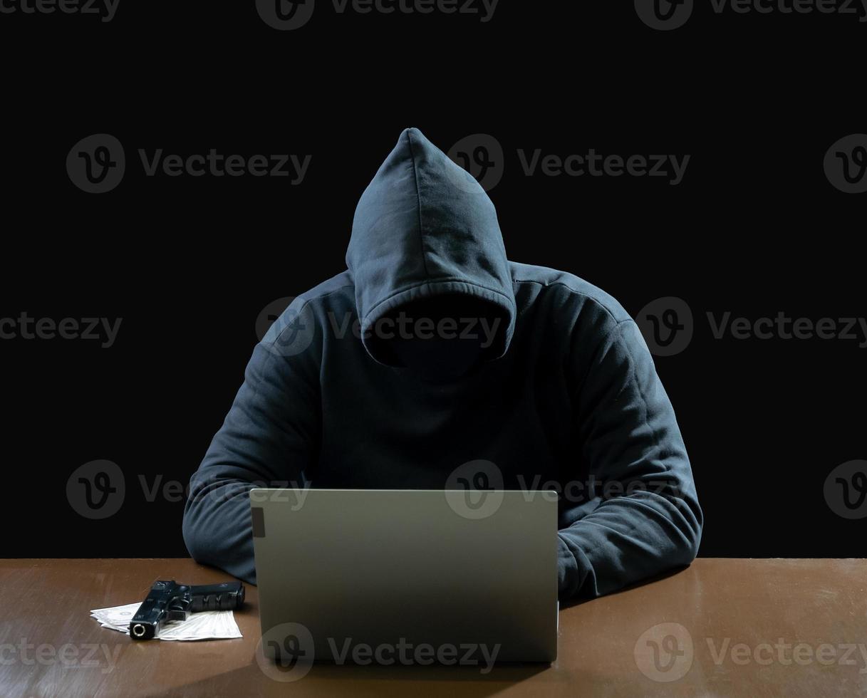Hacker-Spionage-Mann eine Person in schwarzem Kapuzenpulli, die auf einem Tisch sitzt und einen Computer-Laptop ansieht, verwendet Login-Passwort-Angriffssicherheit, um Daten digital im Internet-Netzwerksystem zu zirkulieren, dunkler Hintergrund bei Nacht. foto