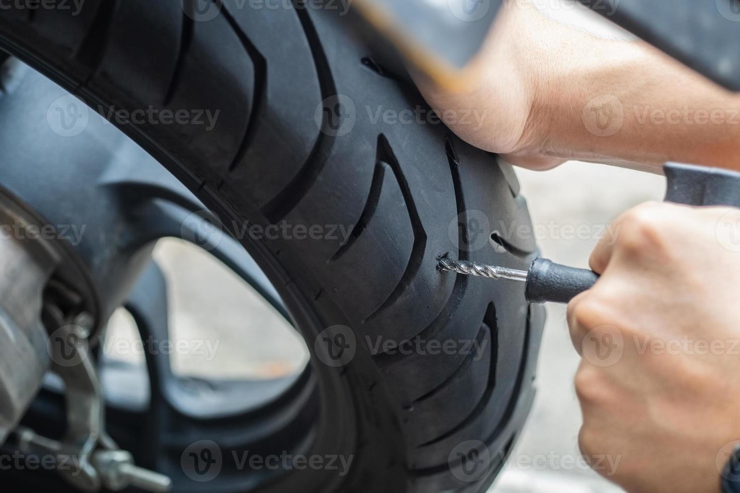 Der Fahrer verwendet ein Reifenstopfen-Kit und versucht, ein Loch in der Seitenwand des Reifens zu reparieren, einen platten Motorradreifen in der Garage zu reparieren. motorradwartungs- und reparaturkonzept foto