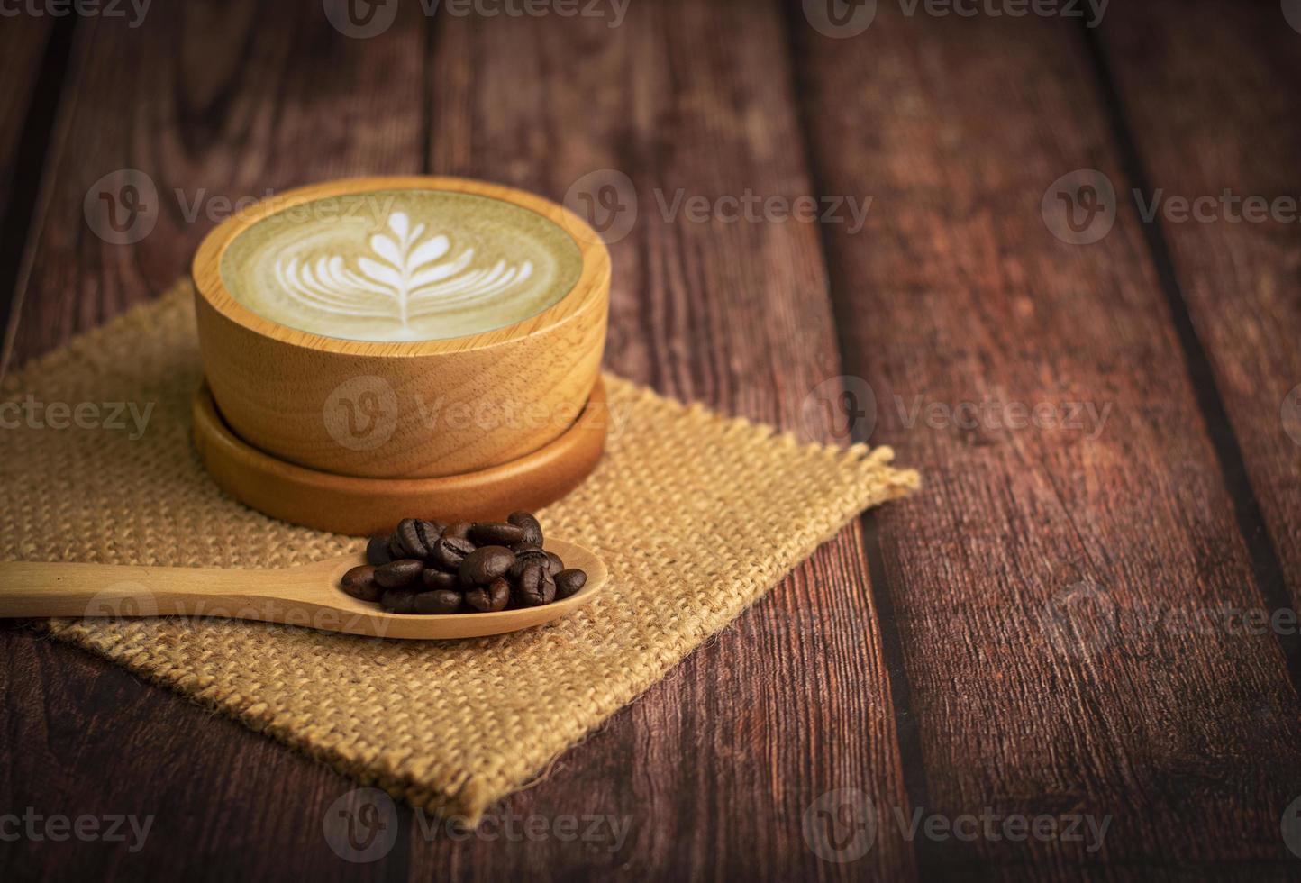 Tasse Kaffee und Latte Art mit Kaffeebohnen im Löffel auf Holztisch foto