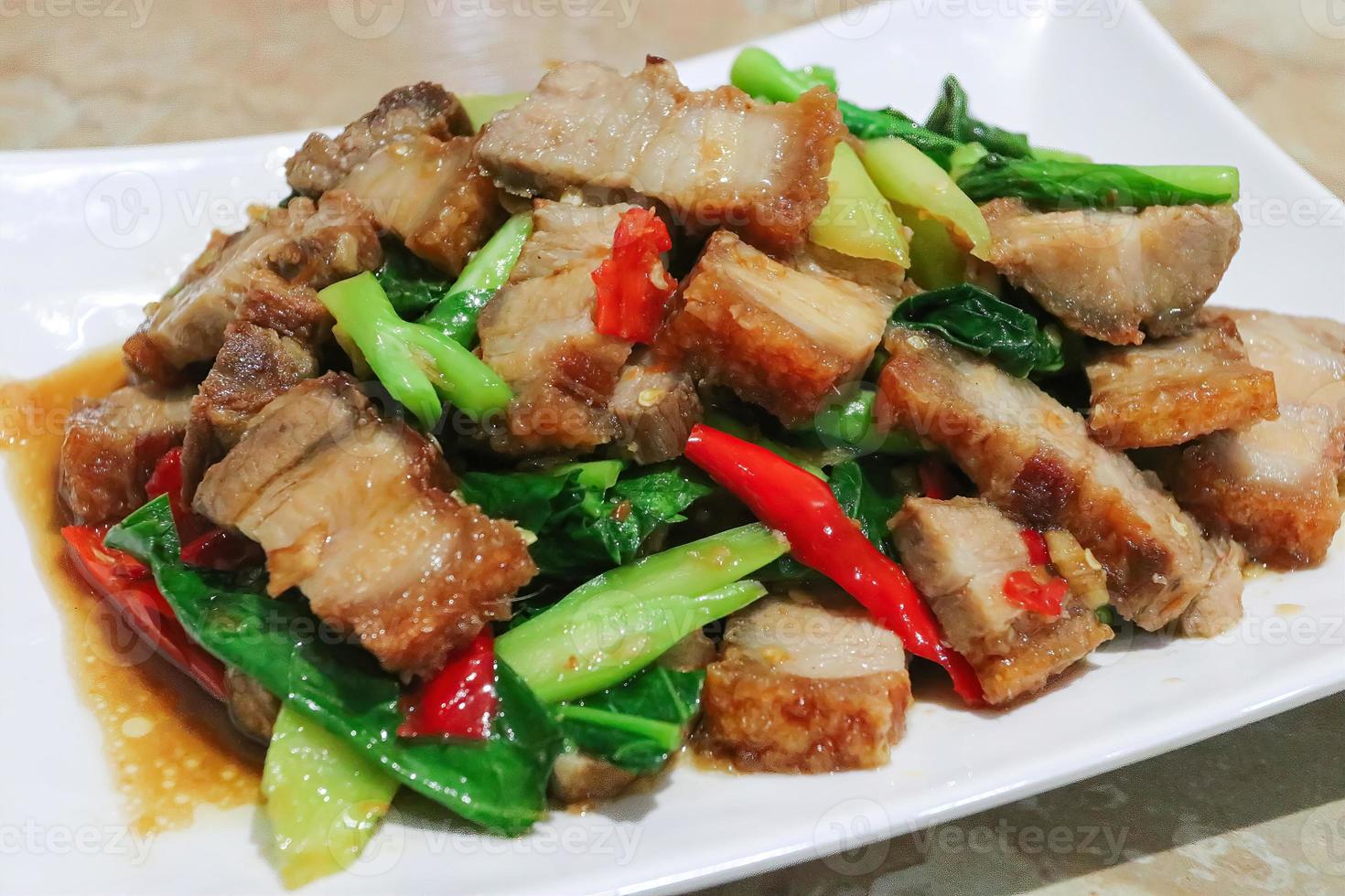 gebratener geschnittener Schweinebauch unter Rühren mit chinesischem Grünkohl auf weißem Teller braten foto