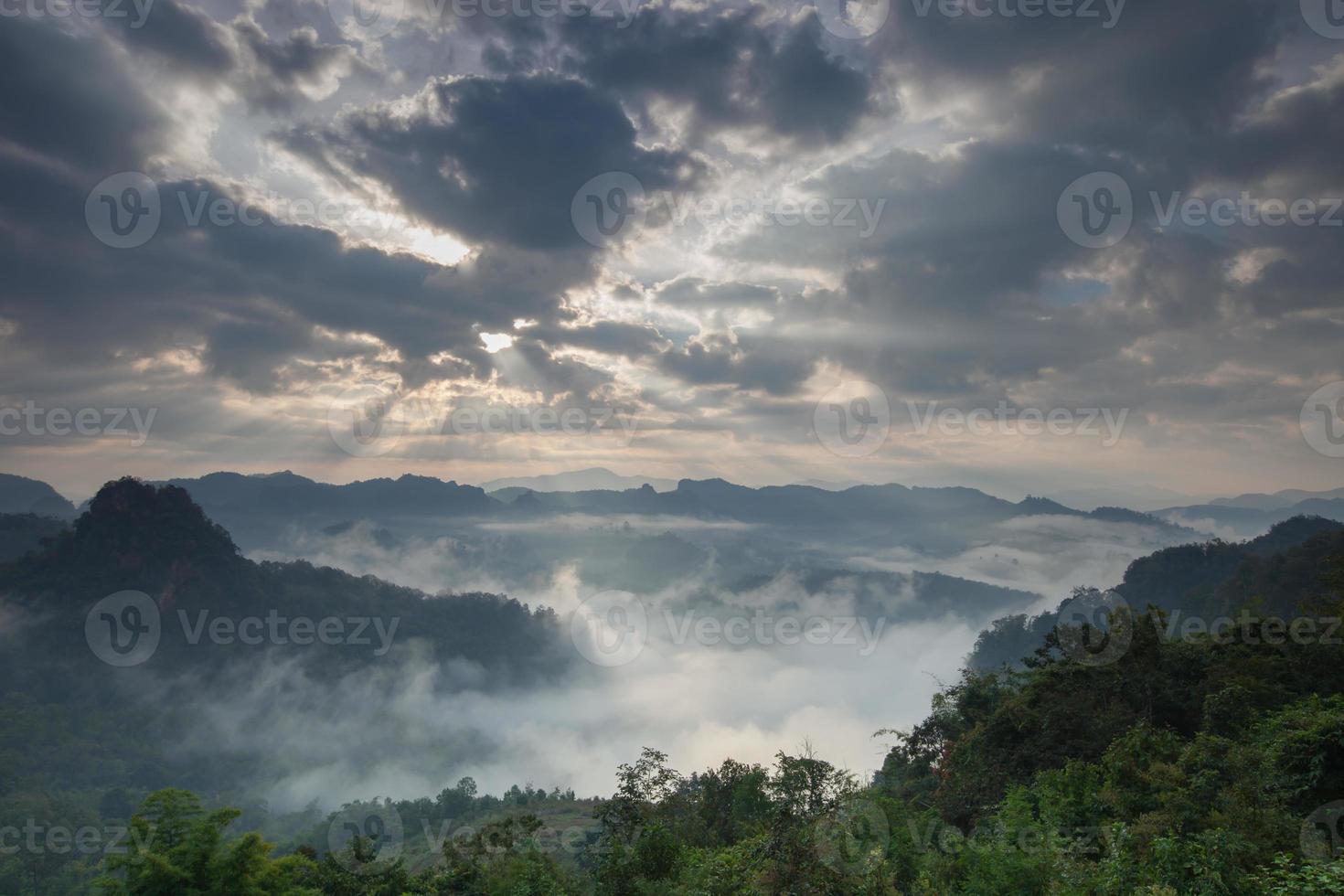 Sonnenaufgang durch Wolken auf nebligen Bergen foto