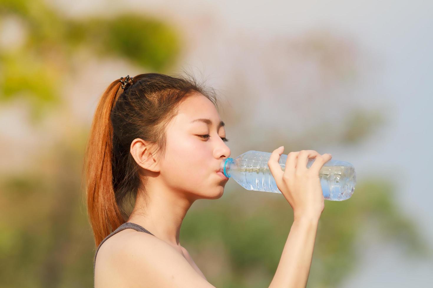 Trinkwasser der sportlichen Frau im Freien am sonnigen Tag foto
