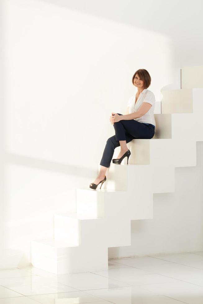Frau lächelt, während sie auf Stufen sitzt foto